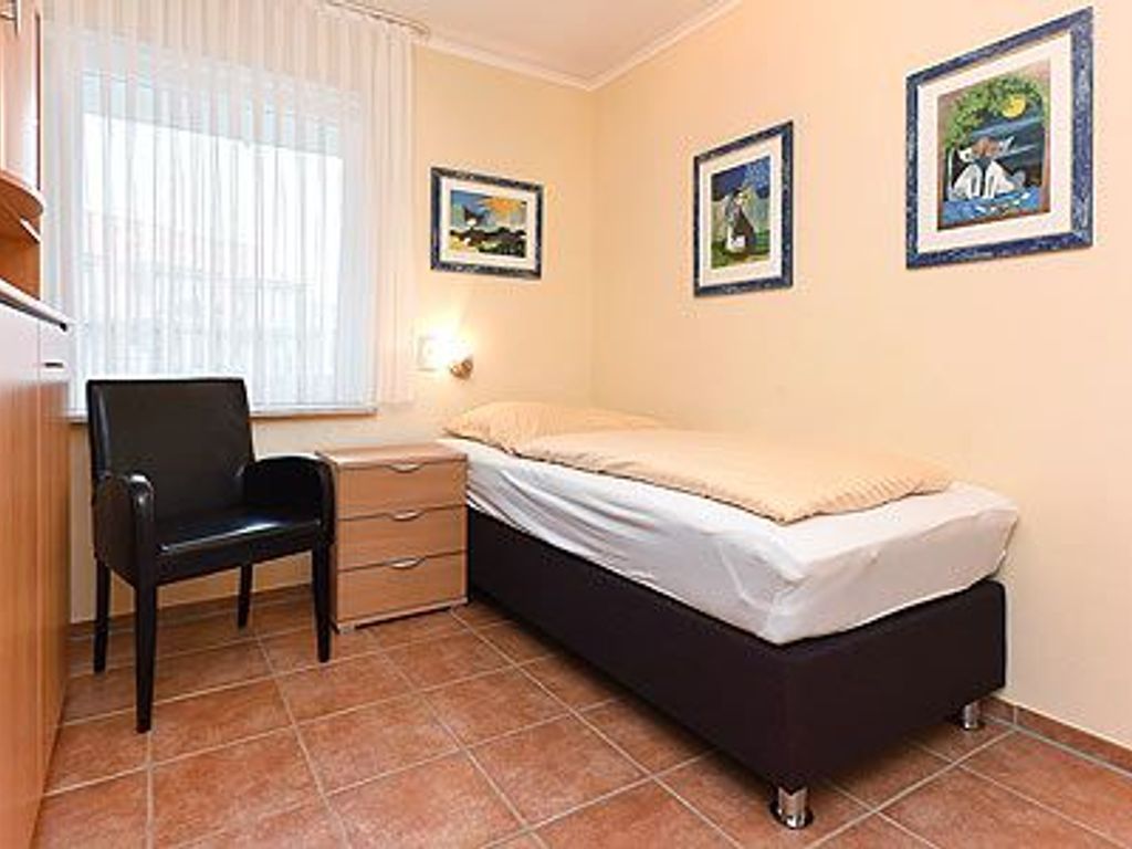 Een slaapkamer met een enkel bed, een stoel, een nachtkastje en een raam met gordijnen.