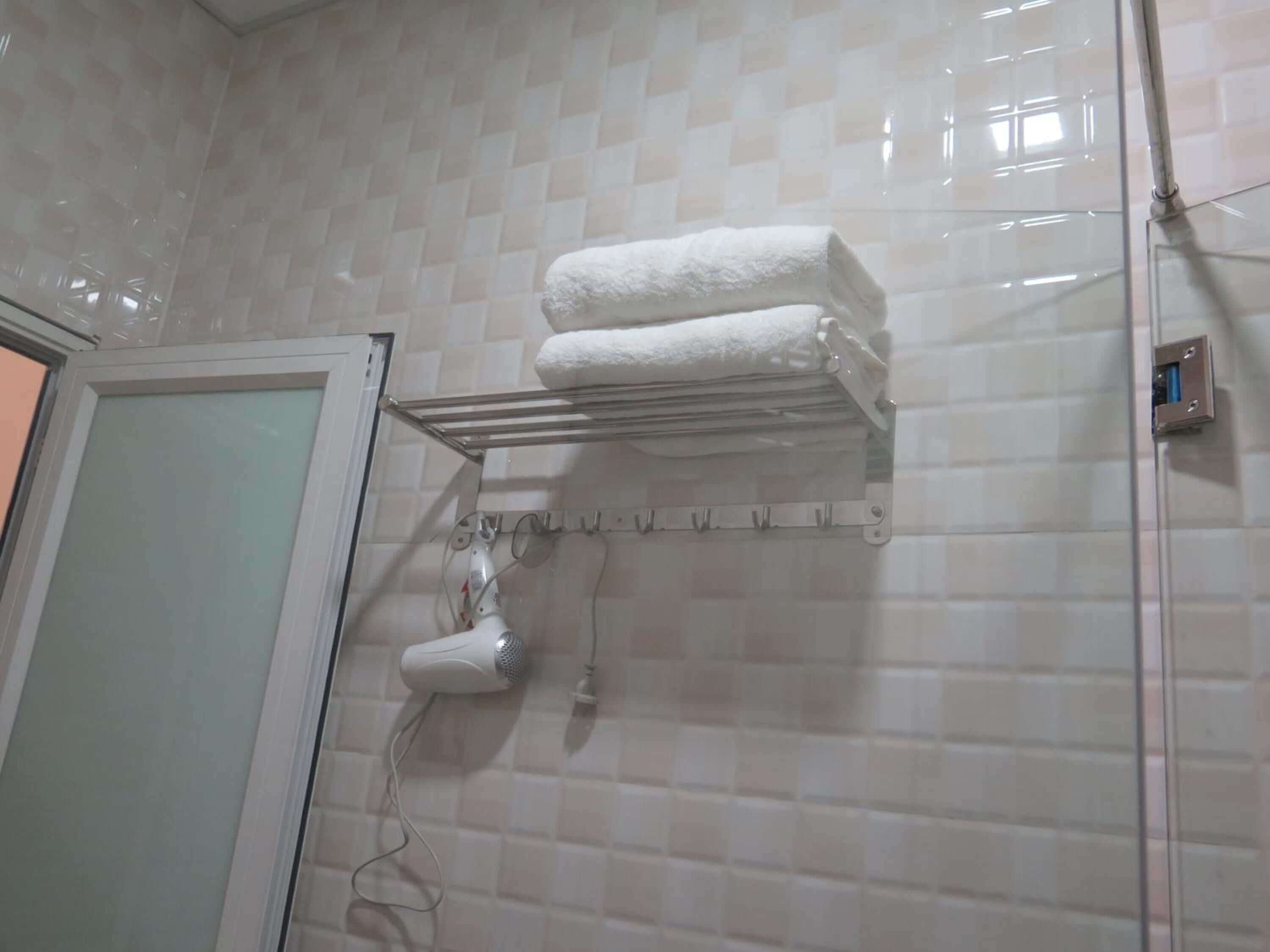 Ein Badezimmer mit Handtuchhalter, zwei gefalteten Handtüchern, einem Fön und einer Duschkabine.