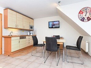 Eine kompakte Küche mit Essbereich, einem an der Wand befestigten Flachbildfernseher und einer Uhr.
