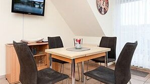 Ein Essbereich mit Tisch und vier Stühlen, einem an der Wand befestigten Fernseher und einer Wanduhr.