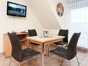 Un'area pranzo con un tavolo e quattro sedie, una televisione montata a parete e una sveglia appesa al muro.