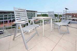 Ein Balkon mit weißen Metallstühlen und einem Tisch, mit Blick auf einen Parkplatz und Gebäude.