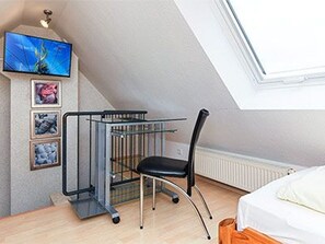 Ein Zimmer mit einem Bett, einem Sessel, einem an der Wand montierten Fernseher und einem Fenster.