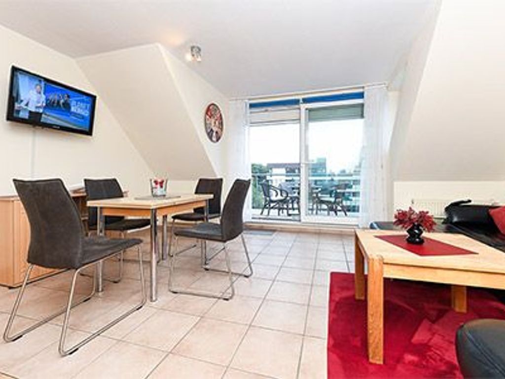 A modern living room with a dining area, a television mounted on the wall, and a balcony with a view.