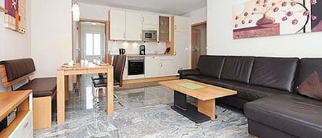 A modern living room with a sofa, coffee table, and a dining area with chairs and a table.