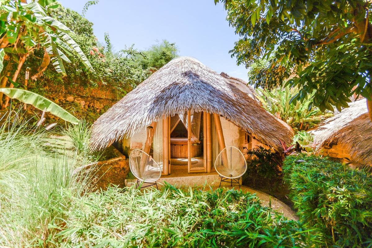 A thatched-roof hut with two wicker chairs in front, surrounded by lush greenery.