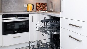Una cucina moderna con mobili bianchi, forno integrato, lavastoviglie e macchina per il caffè.