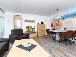 A modern living room with a wooden floor, a dining area with a table and chairs, a sofa, a TV, and a cabinet.