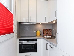 A compact kitchen with white cabinets, a stove, and a sink.