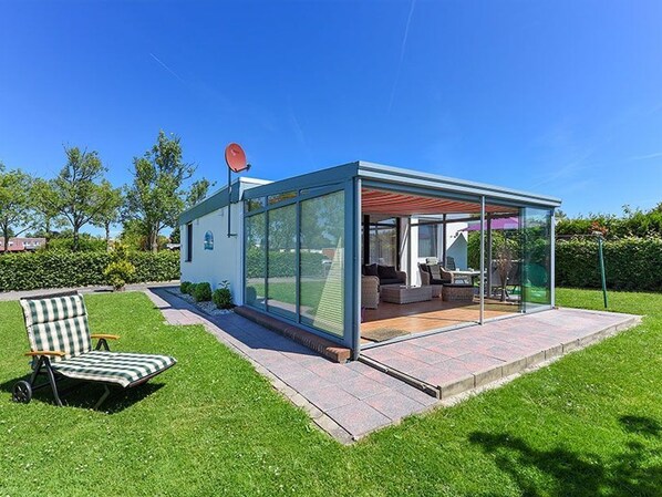 A modern glass house with a patio area, a chair, and a satellite dish.