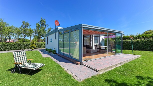 Una moderna casa in vetro con un'area patio, una sedia a sdraio e un'antenna parabolica.