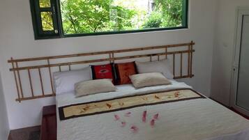 Ein Bett mit Holz-Kopfstück, weißer Bettwäsche und einem Fenster mit Blick ins Grüne.