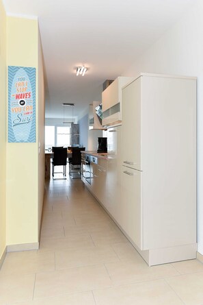 A modern kitchen with white cabinets, a refrigerator, and a dining area with chairs and a table.