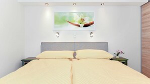 Un letto matrimoniale con copriletto beige, una testiera a fantasia grigia e un quadro di un fiore appeso al muro.