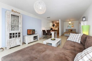 Ein Wohnzimmer mit braunem Sofa, einem Couchtisch, einem Fernseher und einem Schrank mit der Aufschrift 'Relax'.