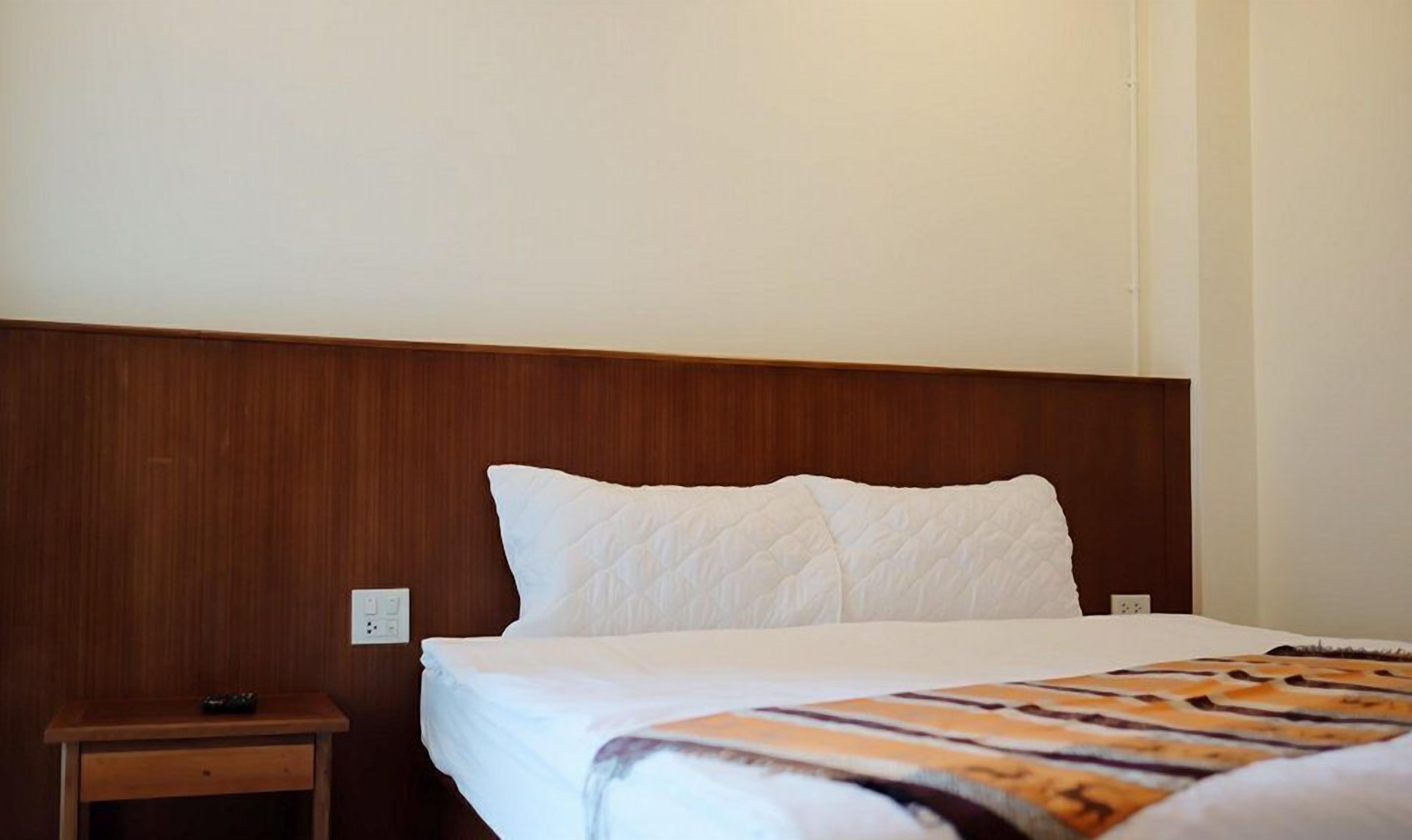 A hotel room with a wooden headboard, a white bedspread, and a nightstand with a remote control.