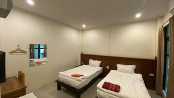 Una habitación de hotel con dos camas individuales, una silla de madera, una mesita y un espejo en la pared.