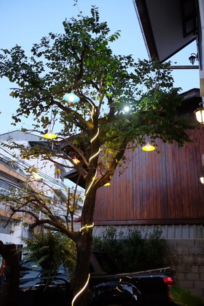 A tree with hanging lights, a wooden building, and parked cars. - Jitra Resort (Sukhothai)