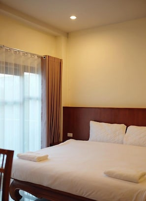 Ein Hotelzimmer mit Bett, Stuhl, Fenster mit Vorhängen und einem Holzkopfteil.