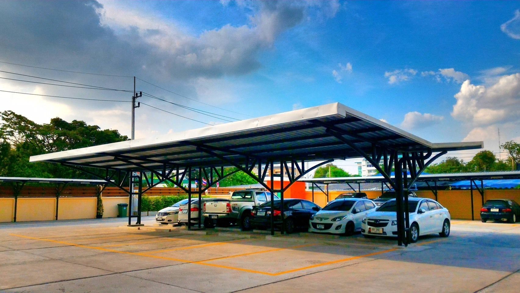 Área de estacionamento coberta com vários carros estacionados sob uma estrutura de metal.