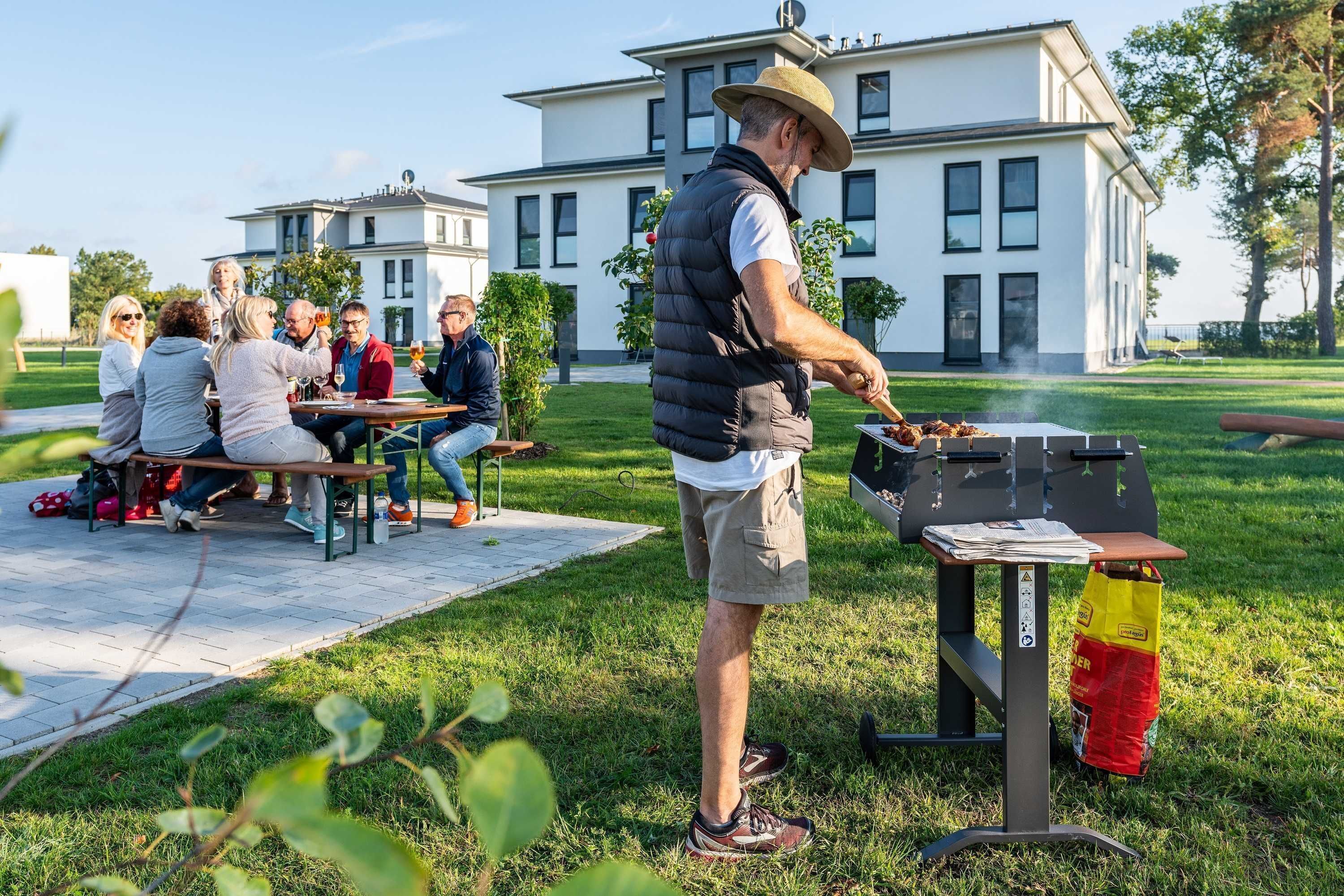 Un grupo de personas reunidas alrededor de una parrilla al aire libre, con un edificio moderno de fondo.