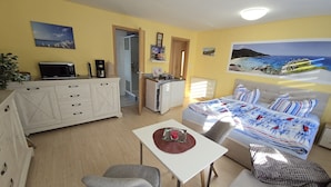 A compact living space with a kitchenette, a dining area, and a bed with a beach-themed mural. - Small Bungalow Wiesenperle - Small Bungalow meadow pearl (Trassenheide)