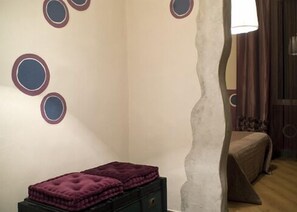 A bedroom with a bed, a nightstand, and a wall with circular decorations. - Hotel Colombo (Genoa)