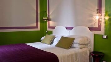A neatly made bed with white bedding and multiple pillows, a green wall with a decorative trim, and a small side table with a vase.