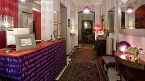 A hotel lobby with a reception desk, a red curtain, a chandelier, and a patterned rug. - Hotel Colombo (Genoa)