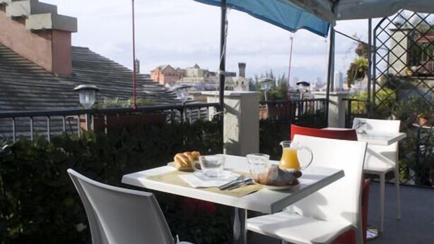 An outdoor dining area with a table set for two, a pitcher of orange juice, and a croissant on the table. - Hotel Colombo (Genoa)