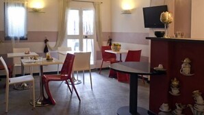A dining area with tables and chairs, a television mounted on the wall, and a decorative tea set on a counter. - Hotel Colombo (Genoa)