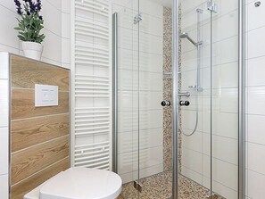 A bathroom with a glass shower enclosure, a white toilet, and a wooden panel wall.