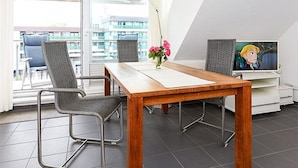 A modern room with a wooden dining table, two metal chairs, a TV, and a balcony with yellow-striped awnings. - Apartment North Sea Sun - North Sea Garden Park North Sea pride (Esens)