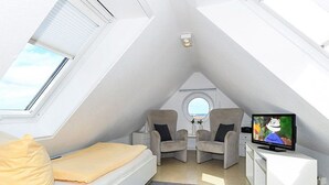 A modern loft bedroom with a skylight, a bed, two armchairs, a small table, and a TV. - Apartment North Sea Sun - North Sea Garden Park North Sea pride (Esens)