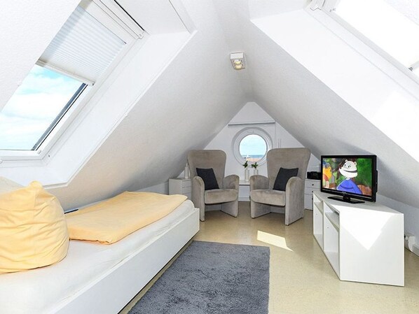 Une chambre de style loft moderne, dotée d’une fenêtre de toit, d’un lit, de deux fauteuils, d’une petite table et d’un téléviseur.