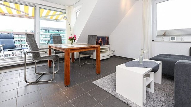 A modern living room with a dining area, a sofa, a TV, and a balcony with a yellow awning. - Apartment North Sea Sun - North Sea Garden Park North Sea pride (Esens)