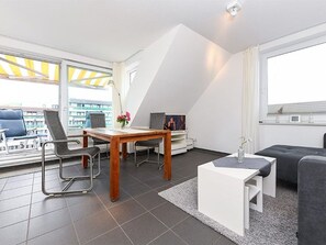 Un salon moderne comprenant un coin repas, un canapé, un téléviseur et un balcon doté d’un auvent jaune.