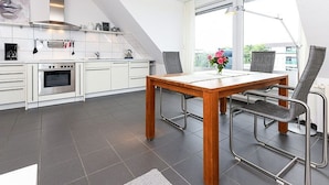 A modern kitchen with white cabinets, a stainless steel range hood, and a dining area with a wooden table and metal chairs. - Apartment North Sea Sun - North Sea Garden Park North Sea pride (Esens)