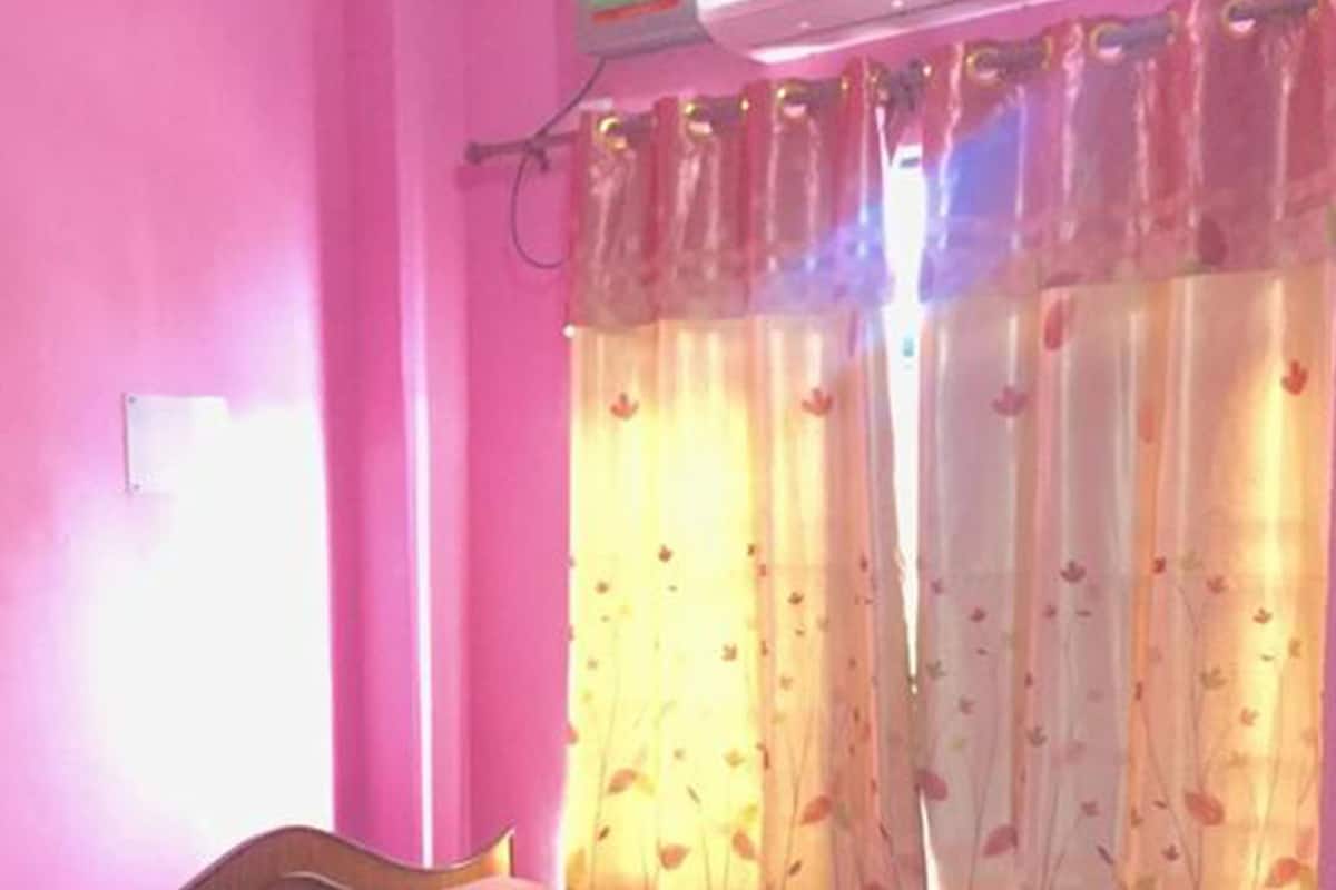 Un dormitorio con cama de madera, paredes rosadas y una ventana con cortinas estampadas.