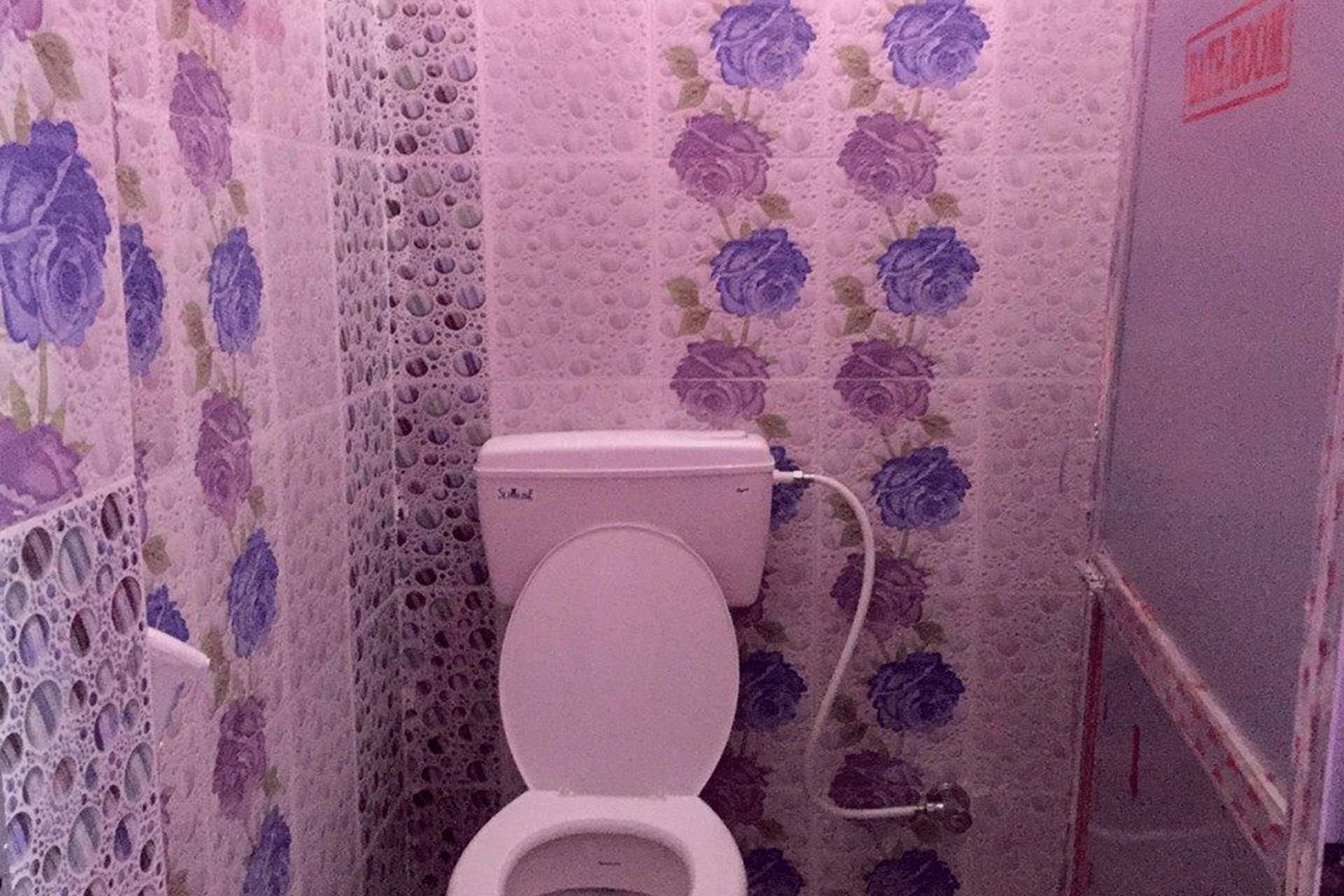 A bathroom with a toilet, a shower area, and floral-patterned walls.