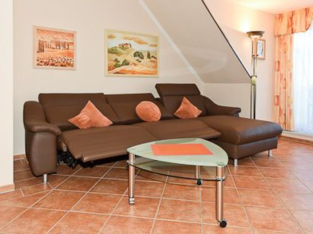 Een moderne woonkamer met een bruine hoekbank, een glazen salontafel en twee aan de muur bevestigde schilderijen.