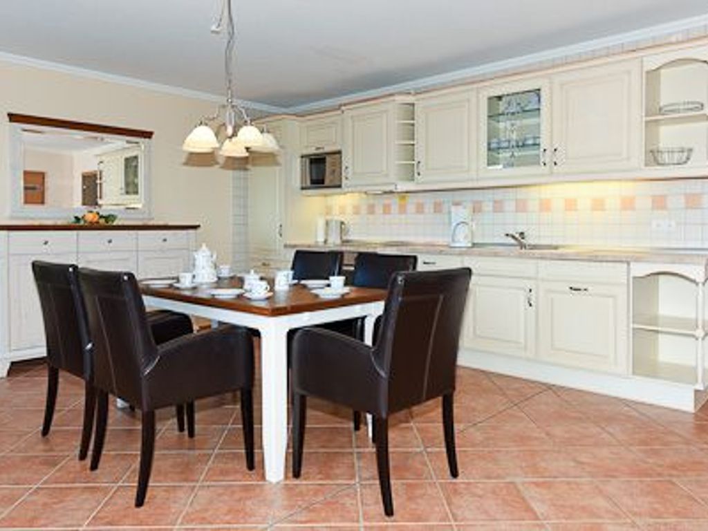 A modern kitchen with white cabinetry, a dining table with chairs, and a hanging light fixture.