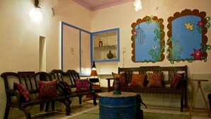 A cozy living room with a wooden bench, a round blue barrel, and a sofa with colorful cushions. - goStops Jodhpur - Hostel (Jodhpur)