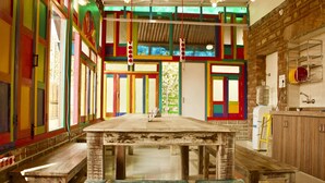 A rustic kitchen with a wooden table, colorful stained glass windows, and a brick wall. - goStops Jodhpur - Hostel (Jodhpur)