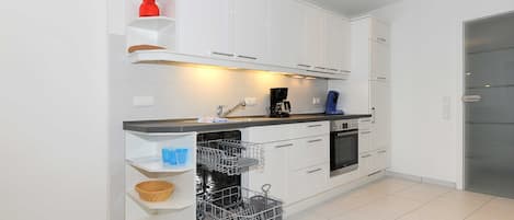 Ett modernt kök med vita skåp, diskmaskin och kaffebryggare.