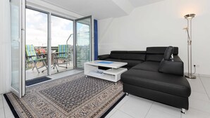 Uma sala de estar moderna com um sofá preto, uma mesa de centro branca e um tapete estampado.