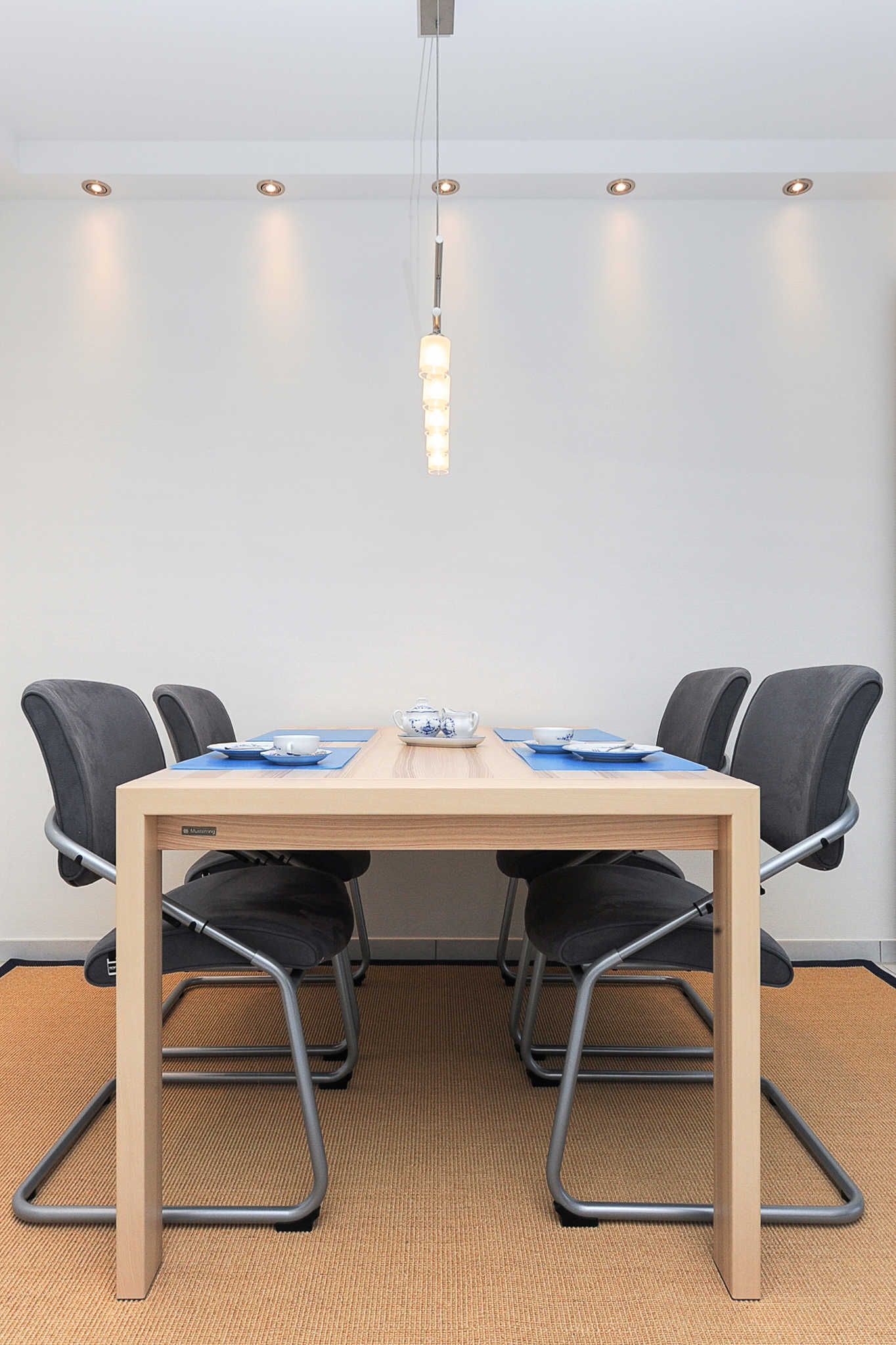 A conference room with a wooden table, four black chairs, and a hanging light fixture.