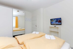 A hotel room with two beds, a television, a wardrobe, and a mirror. - Vacation apartment Benser Nest - Residence Hafenidyll (Esens)