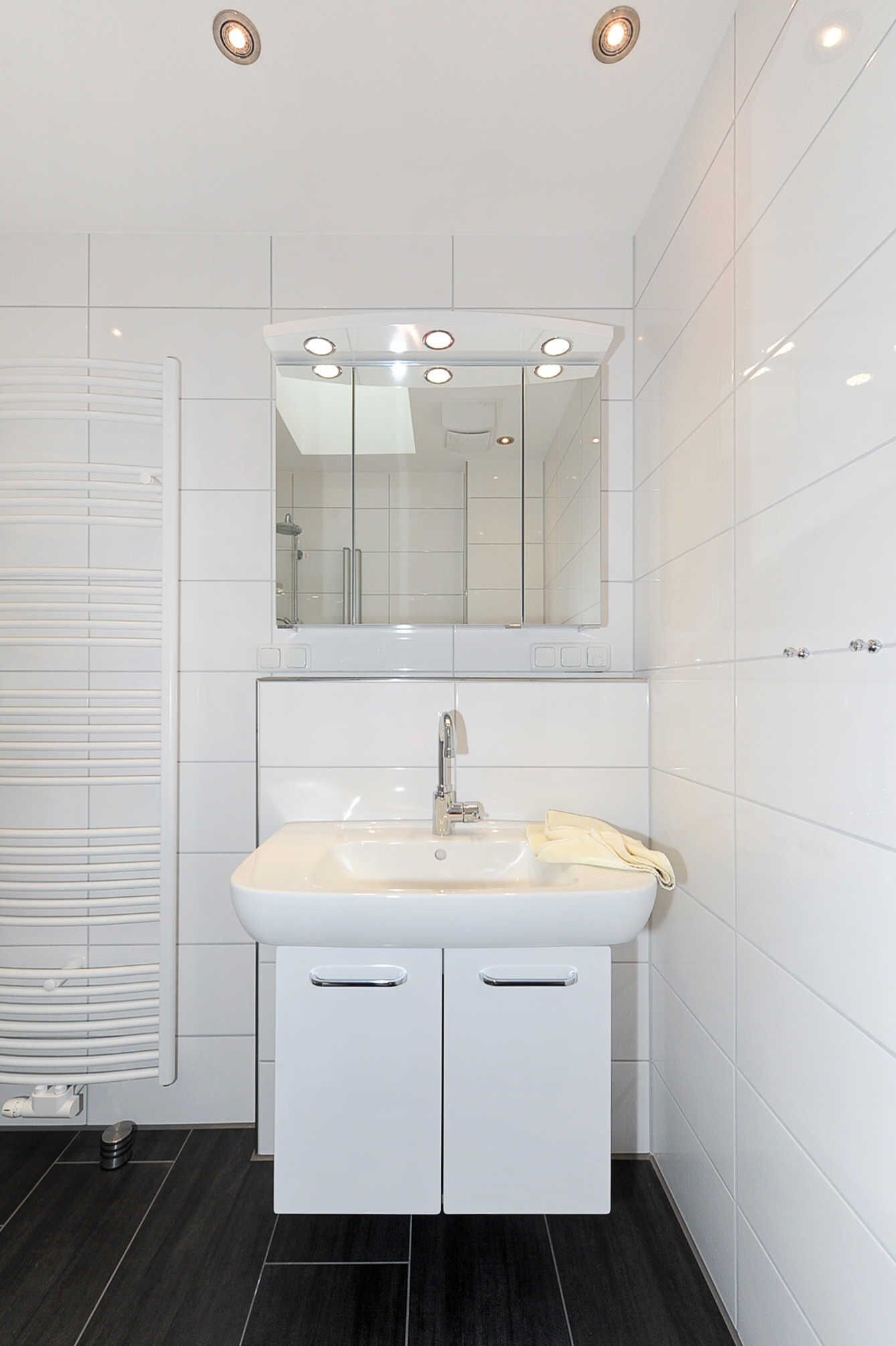A modern bathroom with a white sink, mirror, and tiled walls.