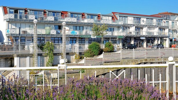 Um edifício de vários andares com varandas, uma placa com 'FISCHERSTUBEN' e uma ponte com grades.